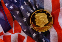 A gold commemorative coin featuring a profile of Donald Trump on an American flag background