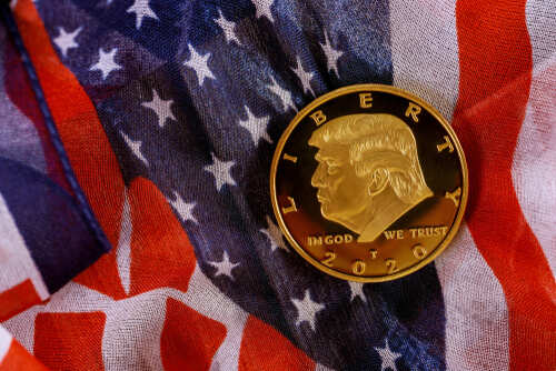 A gold commemorative coin featuring a profile of Donald Trump on an American flag background
