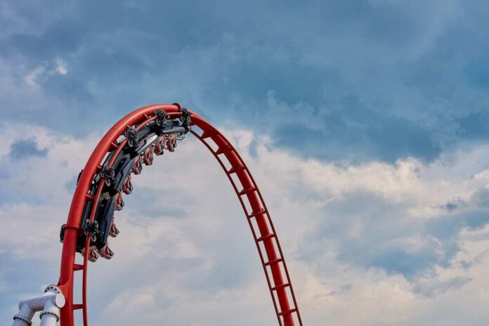 Theme,Park,Energylandia,In,Zator,,Poland.,People,Riding,At,Roller Red roller coaster loop against a cloudy sky