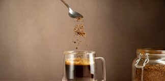 Spoon sprinkling instant coffee granules into a glass cup