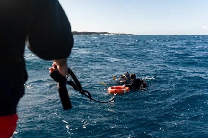 Two scuba divers in the ocean being assisted by a person holding a rescue line