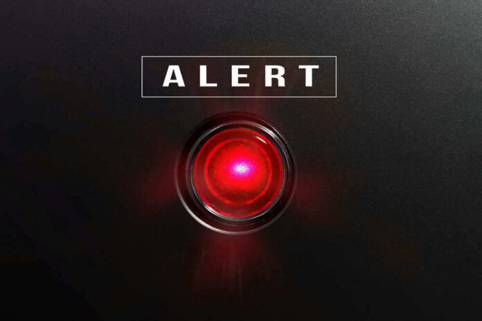 shutterstock_582441490-1 Red alert light against black background, text ALERT.